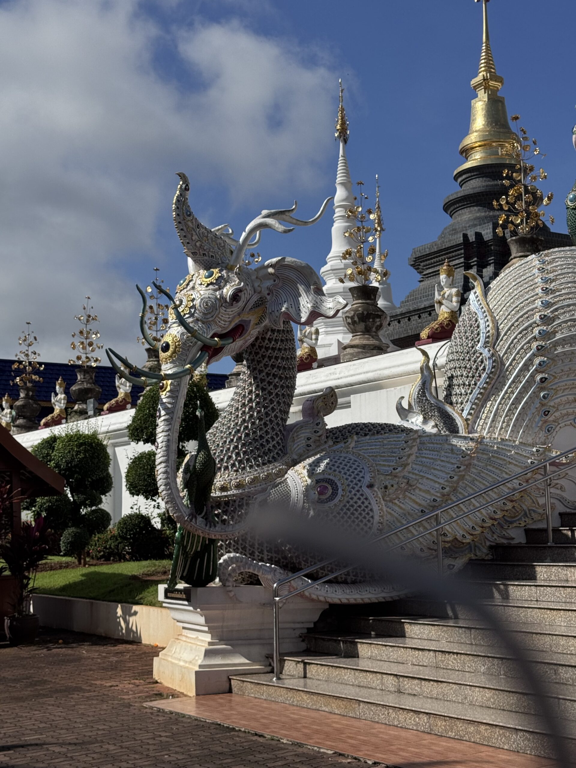 Intricate dragon sculpture adorned with jewels and gold accents, in front of a temple with striking pagodas, showcasing cultural artistry.